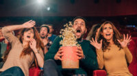 Young people shouting and spilling popcorn when watching a movie at cinema Young People Shouting And Spilling Popcorn When Watching A Movie At Cinema